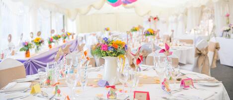 A banquet hall with round tables set for a formal event, decorated with colorful paper lanterns and floral centerpieces.