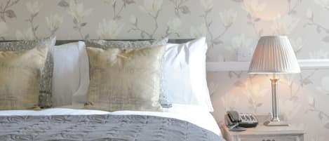 Una cama bien hecha con ropa de cama estampada, una lámpara de noche y una mesita de noche con un teléfono.