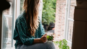 A person sitting by a window with a view of greenery and a brick wall. - Long John’s Hotel (Amersfoort)