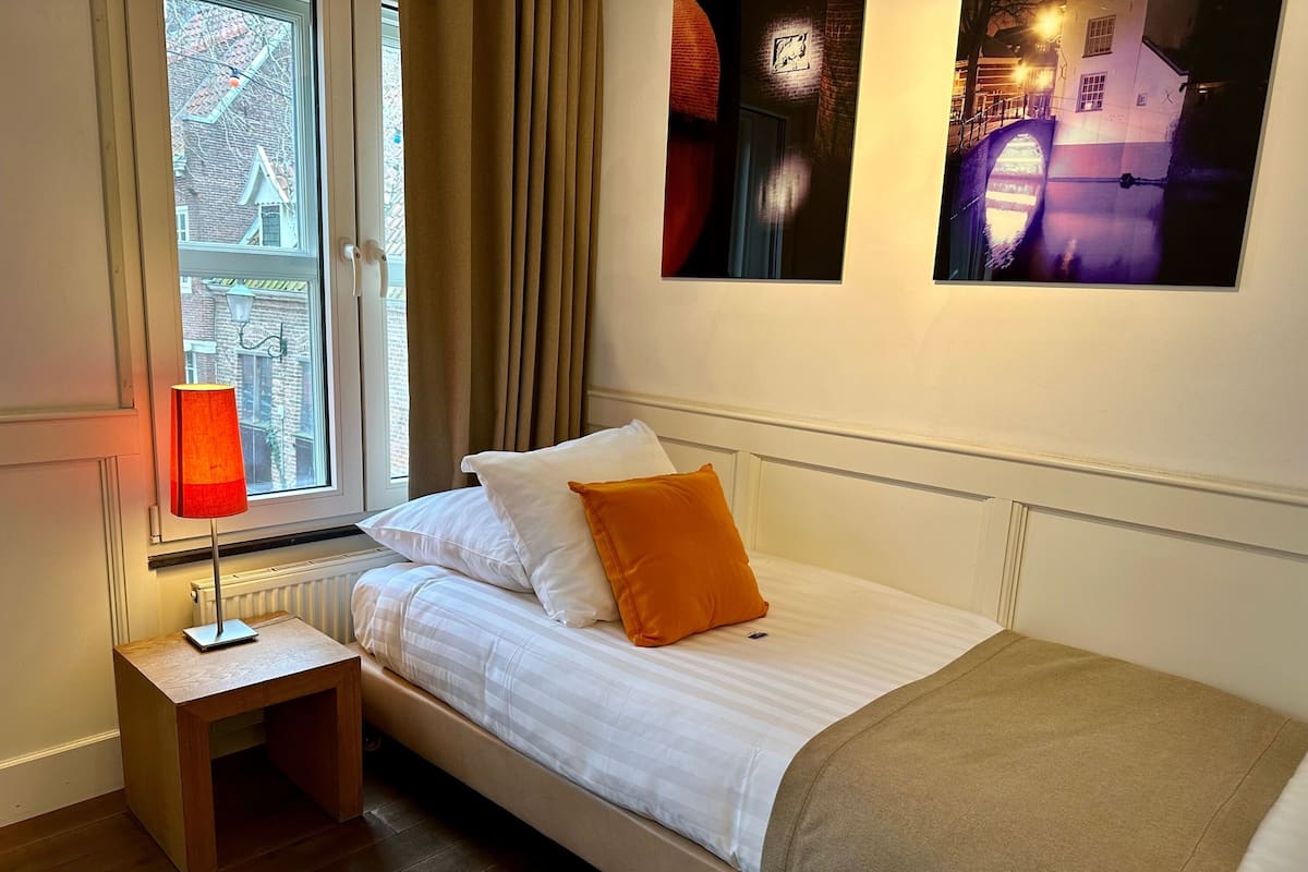 Un dormitorio con cama, mesita de noche, lámpara y ventana con cortinas.