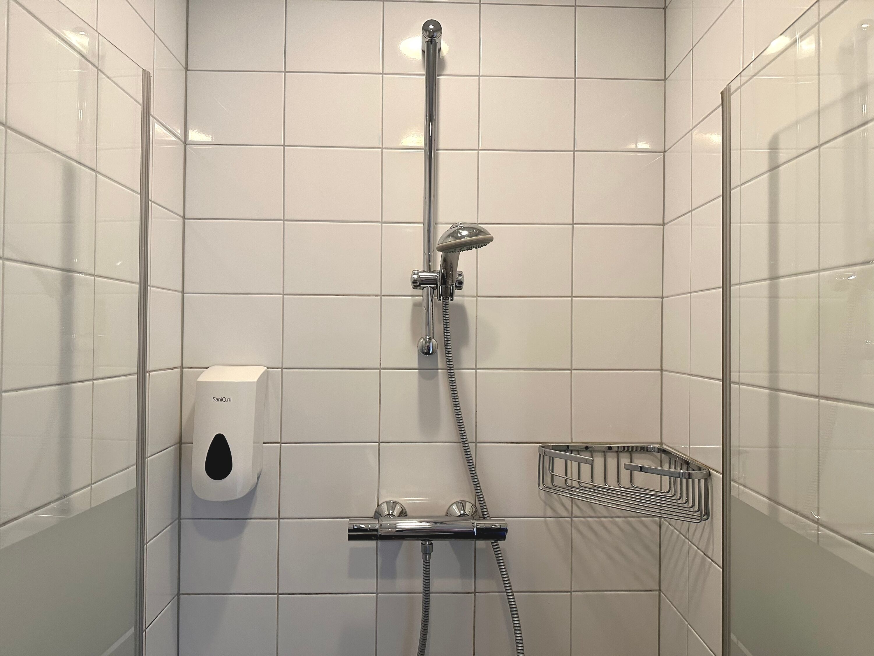 Una ducha moderna con cabezal de ducha manual y un cabezal de ducha fijo, dispensador de jabón y un perchero metálico para toallas.