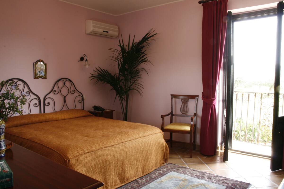 Un dormitorio con cama, una silla, una planta en maceta y un balcón con vistas.