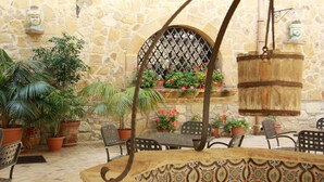 Une terrasse extérieure avec des murs en pierre, des plantes en pot, une table en métal avec des chaises et une lanterne suspendue.
