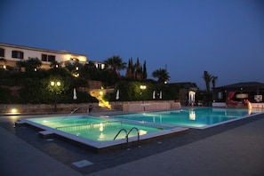 A swimming pool area with two pools, outdoor seating, and a building in the background.
