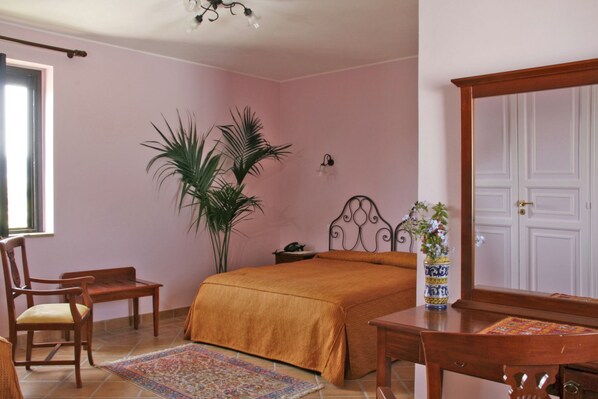 A bedroom with a bed, a chair, a desk, a potted plant, and a door.