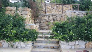 Un escalier en pierre avec des rampes métalliques, entouré d’une végétation luxuriante et de fleurs blanches.