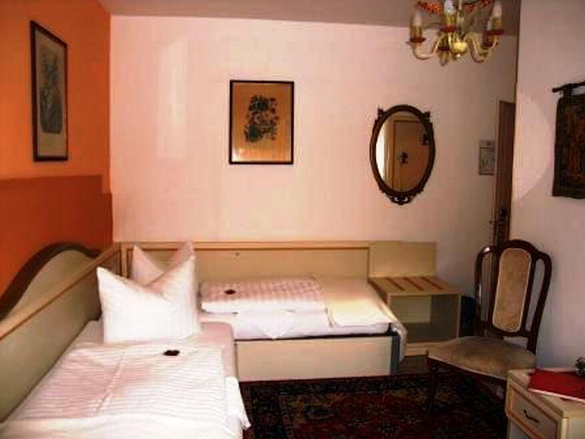 Una habitación de hotel con dos camas, una mesita de noche, una silla, un espejo y una araña.