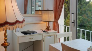 Een hotelkamer met een bureau, een lamp, een spiegel en uitzicht op groen.