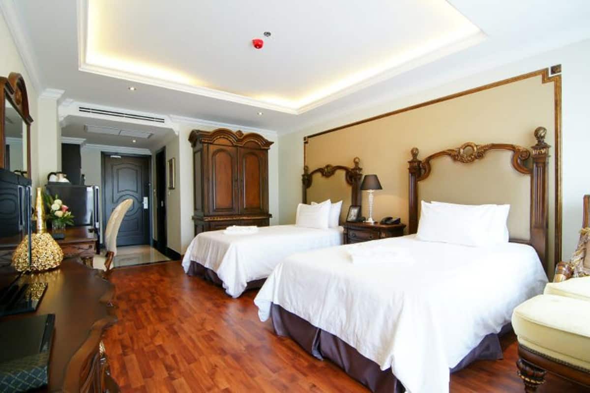 A hotel room with two beds, wooden furniture, and a chandelier.