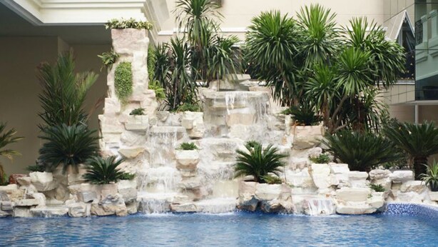 Uma piscina com cascata, rodeada por pedras e plantas tropicais.