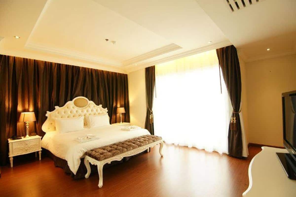 A spacious bedroom with a large bed, a bedside table, a television, and a window with curtains.