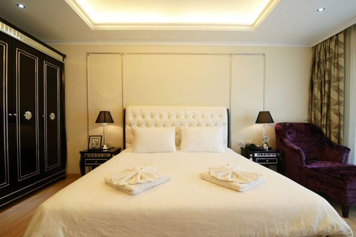 A hotel room with a large bed, two bedside tables with lamps, a wardrobe, and a purple armchair.