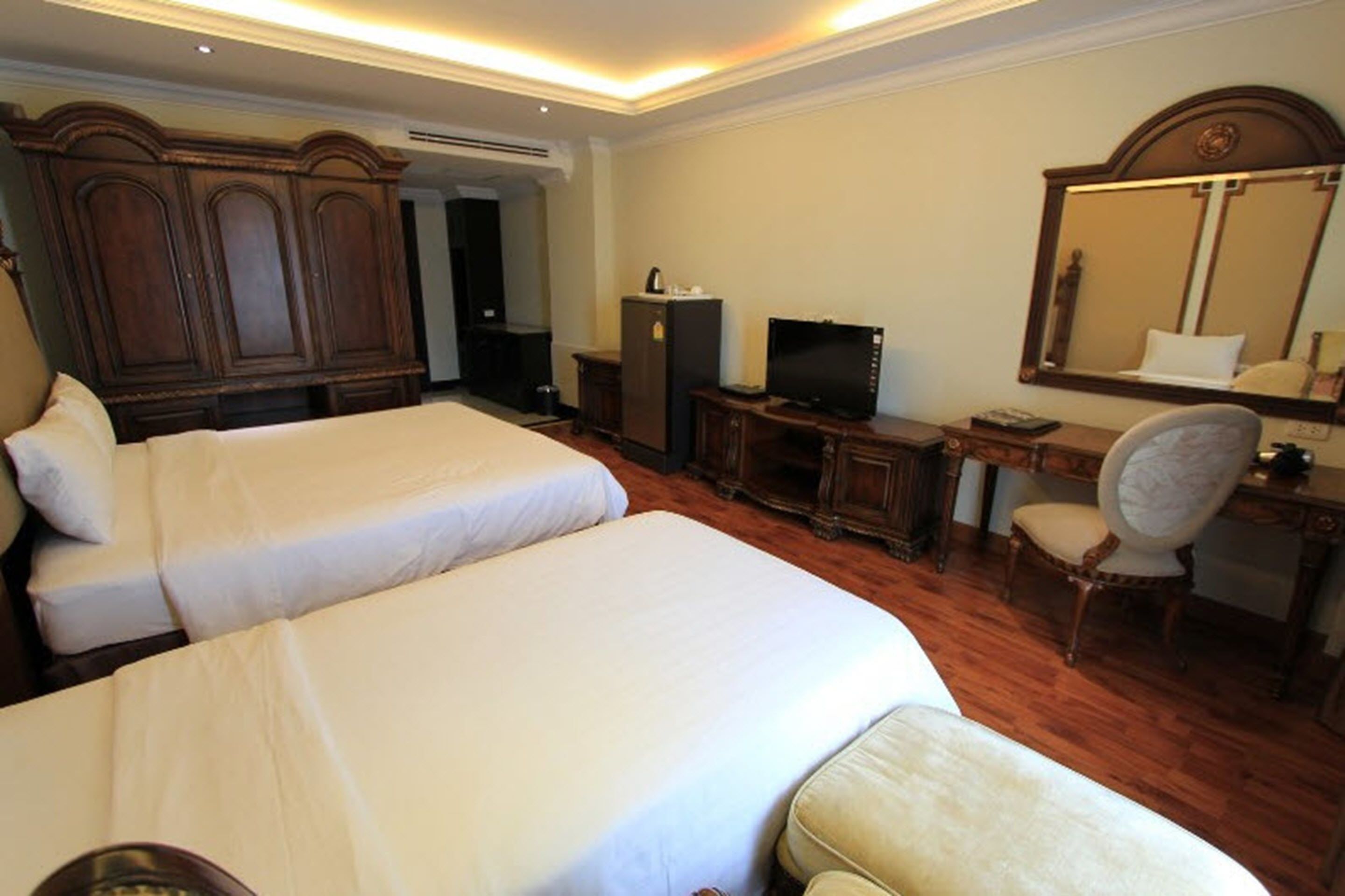 A hotel room with two beds, a desk with a computer, a television, and a large mirror.