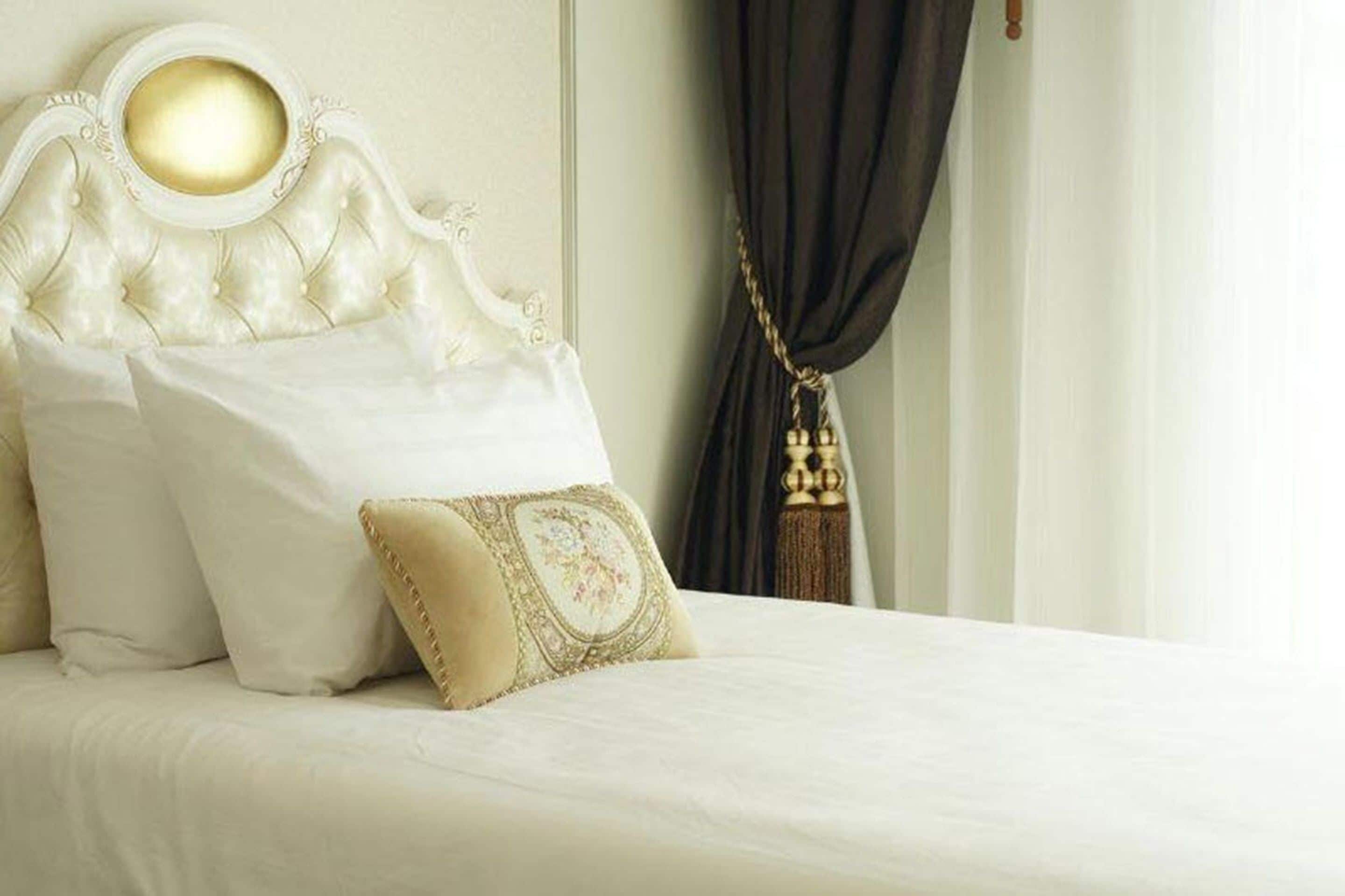 A bed with a tufted headboard, a white pillow, and a decorative pillow with a tassel.