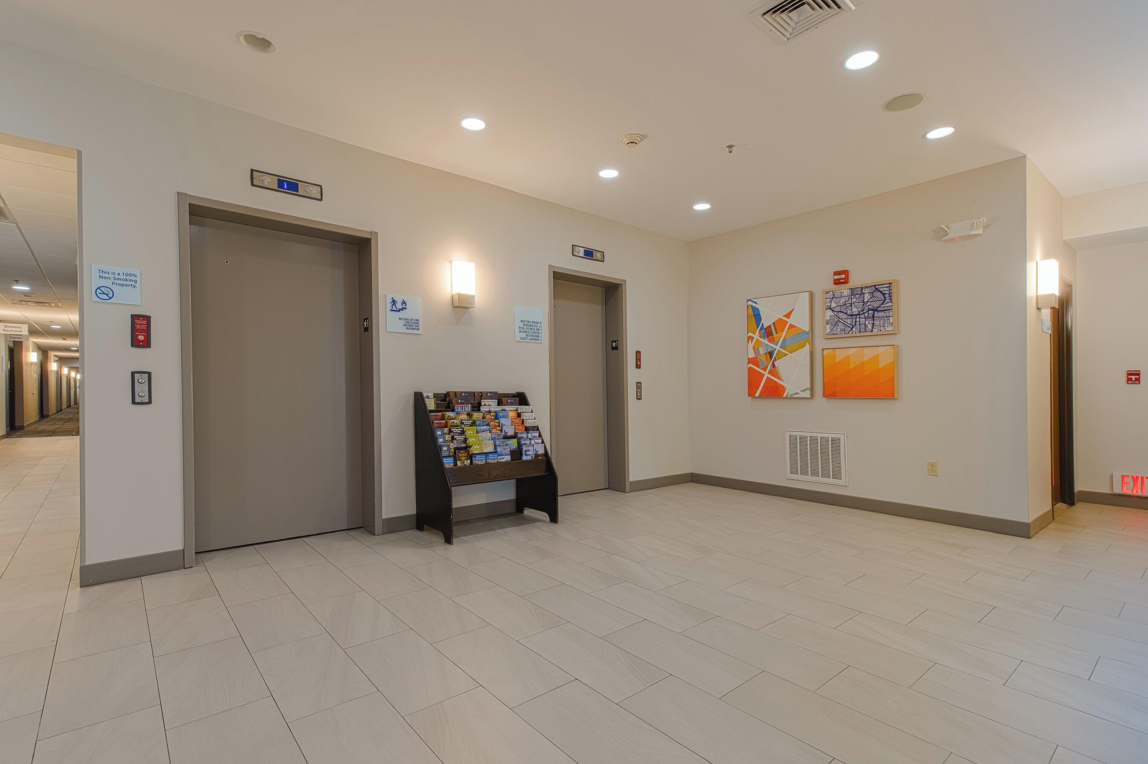 A hallway with a bulletin board, doors, and wall-mounted signs.