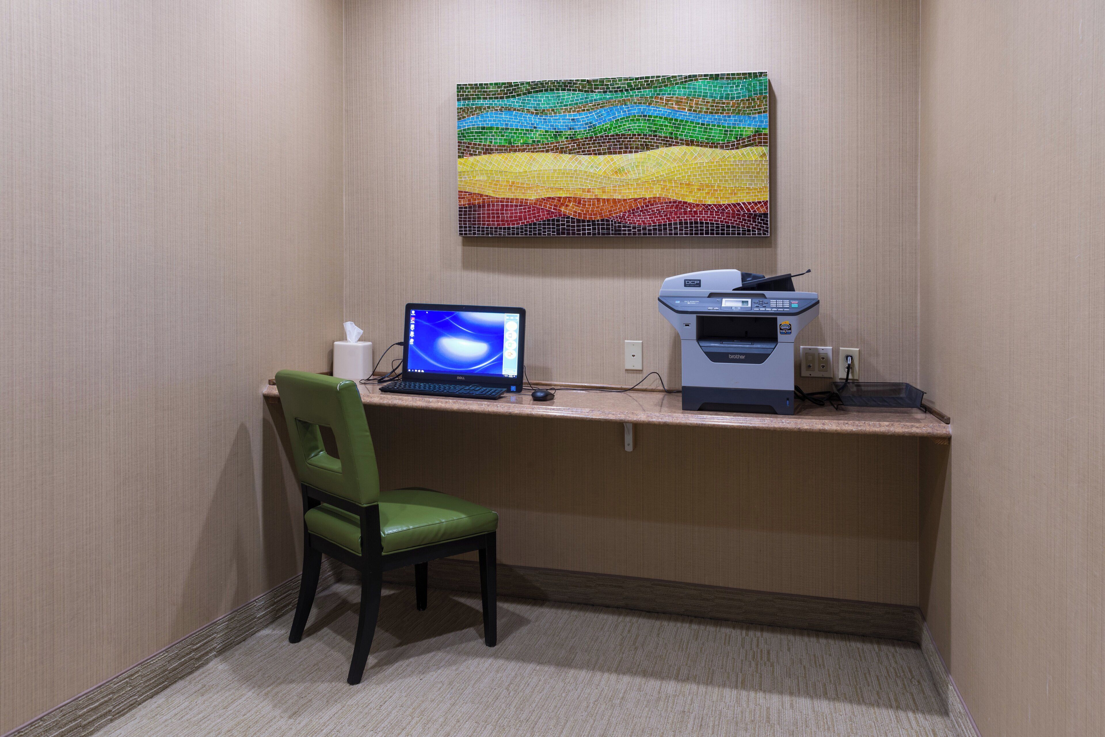Habitación de hotel con escritorio, computadora, impresora, silla y una obra de arte colgada en la pared.