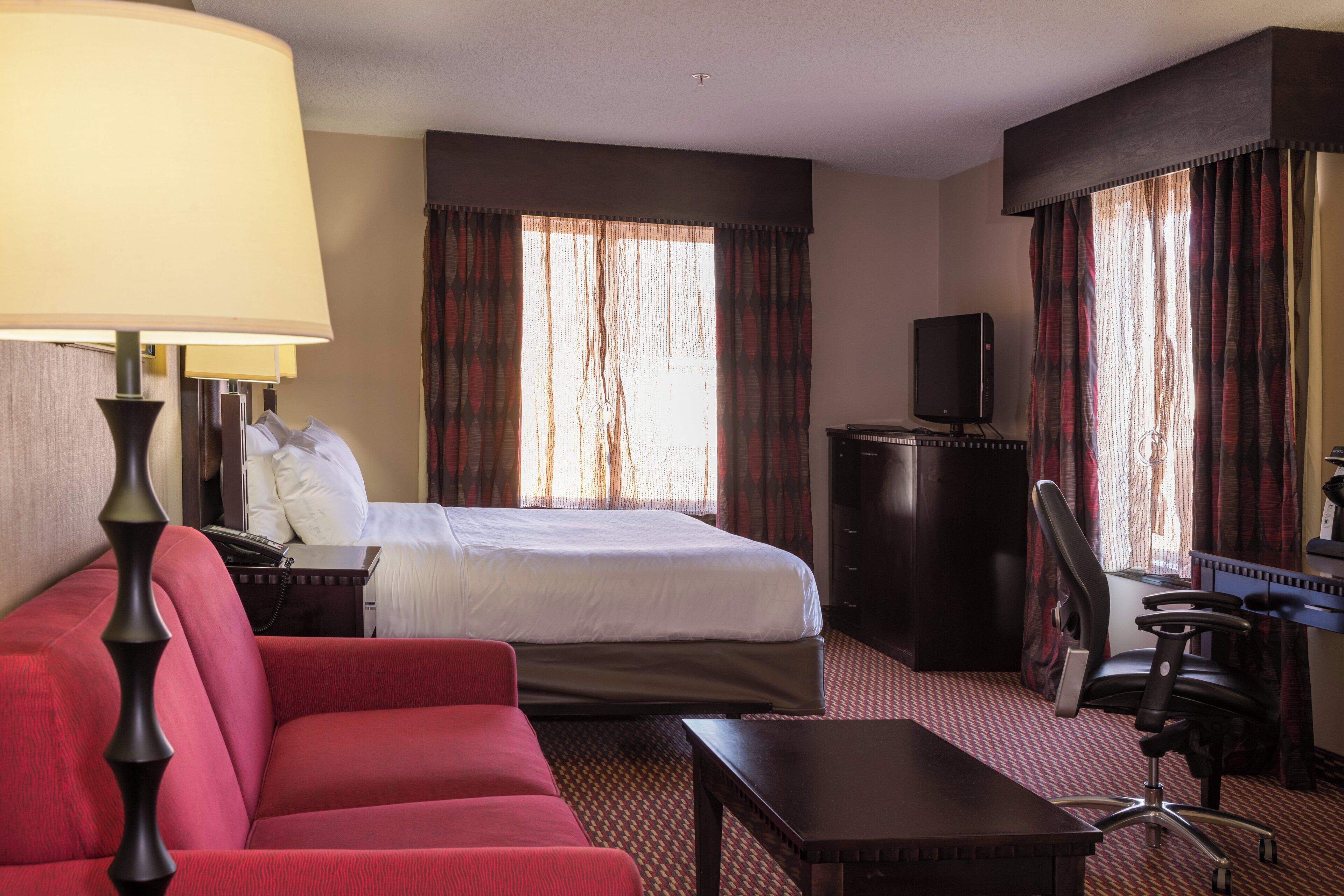 Ein Hotelzimmer mit Bett, Schreibtisch, Stuhl, Fernseher und Lampe.