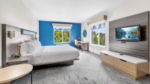 A modern hotel room with a bed, a TV, a desk, and a view of the outdoors.