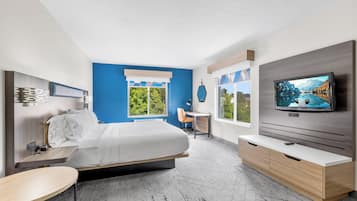 A modern hotel room with a bed, a TV, a desk, and a view of the outdoors.