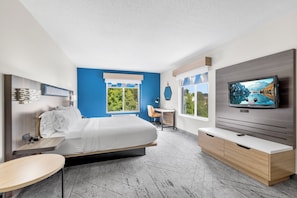 Une chambre d’hôtel moderne équipée d’un lit, d’une télévision, d’un bureau et offrant une vue sur l’extérieur.