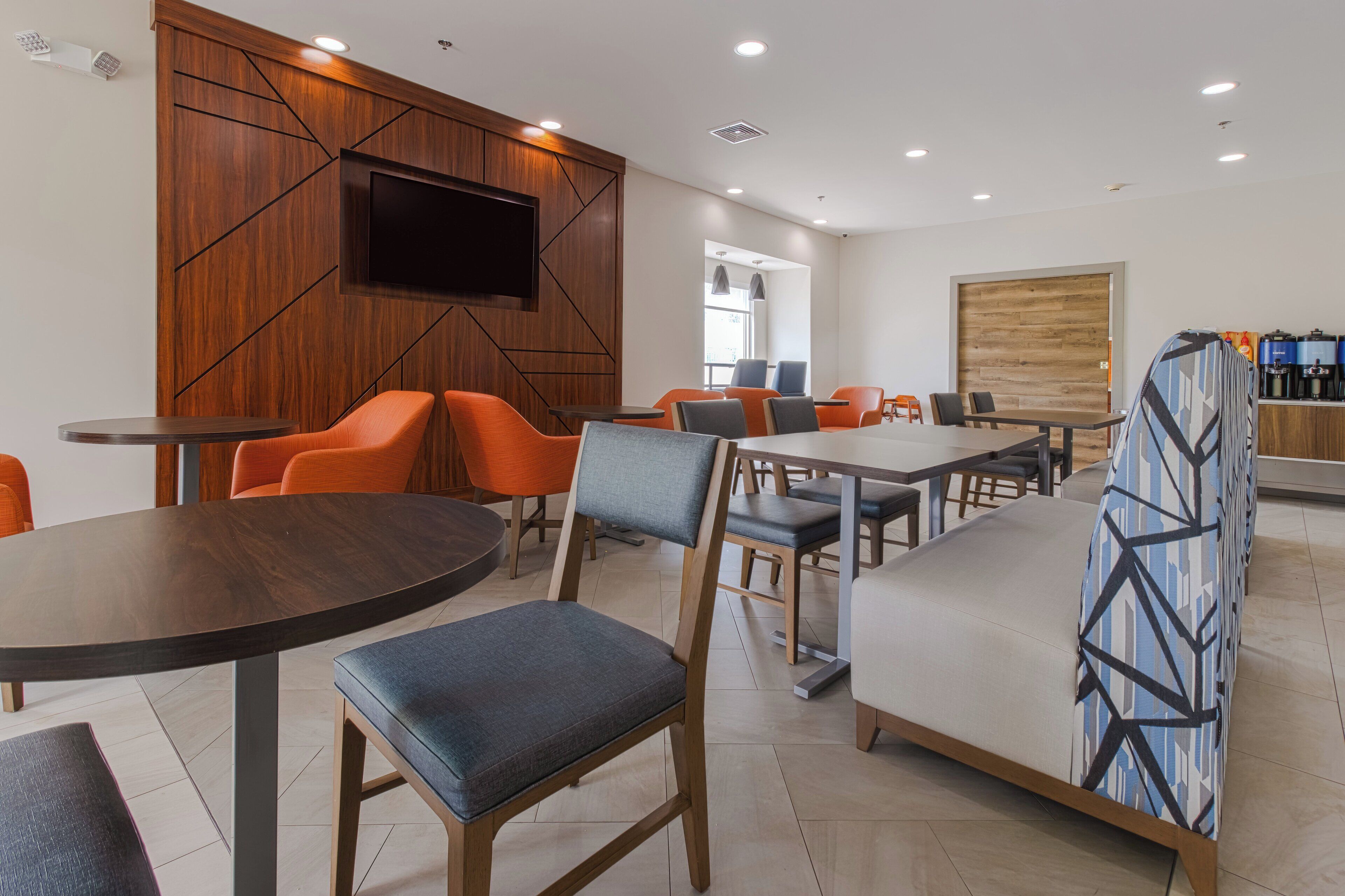 Un comedor moderno con paneles de madera, un televisor de pantalla plana y diferentes opciones de asientos, incluyendo mesas redondas y sofás.