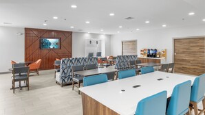 Ein moderner Konferenzraum mit langem Tisch, blau-grauen Stühlen und einer Wand mit Holzpaneelen und einem Fernseher.