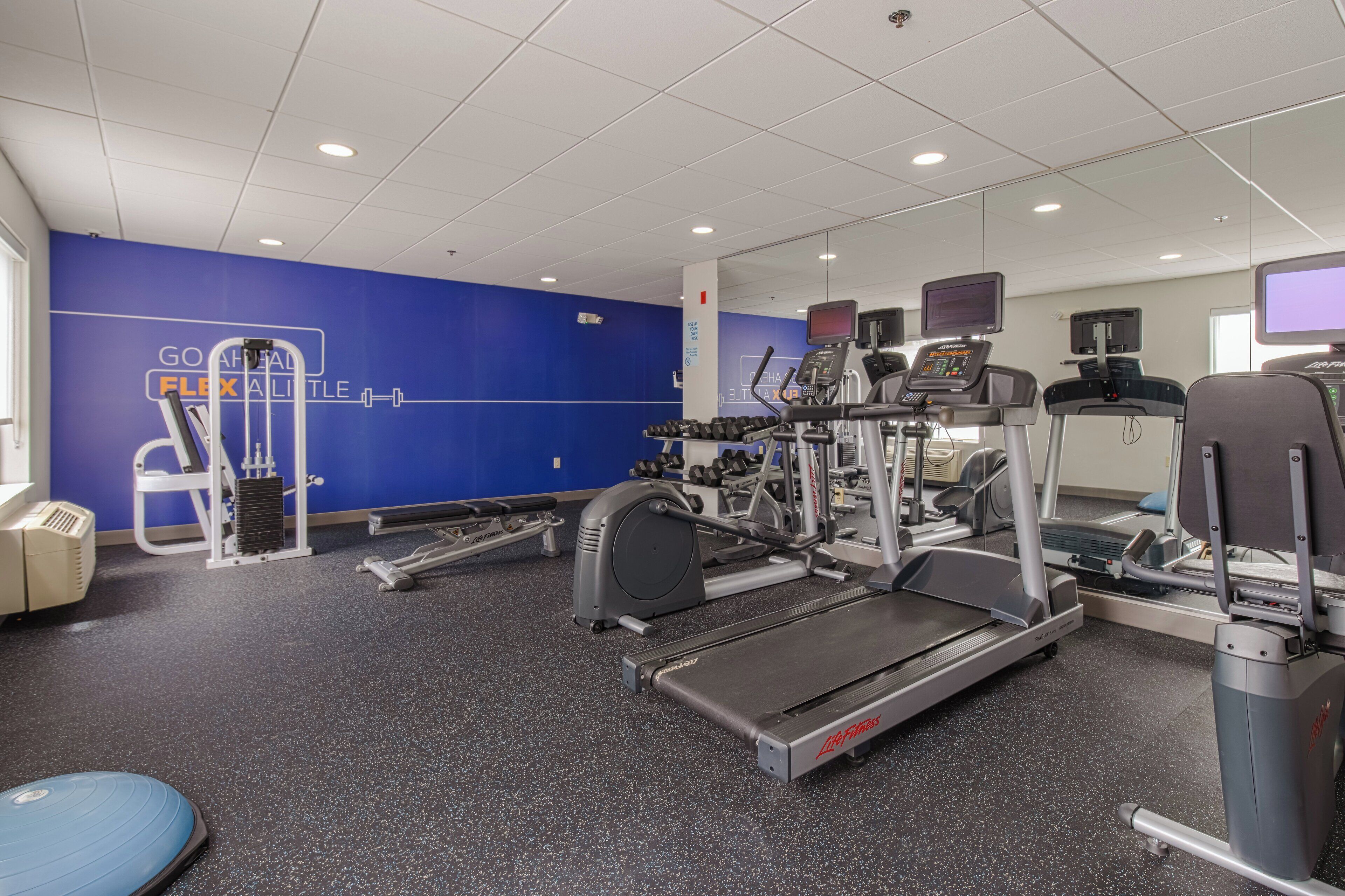 A gym with cardio equipment, weight machines, and a blue wall with motivational text.