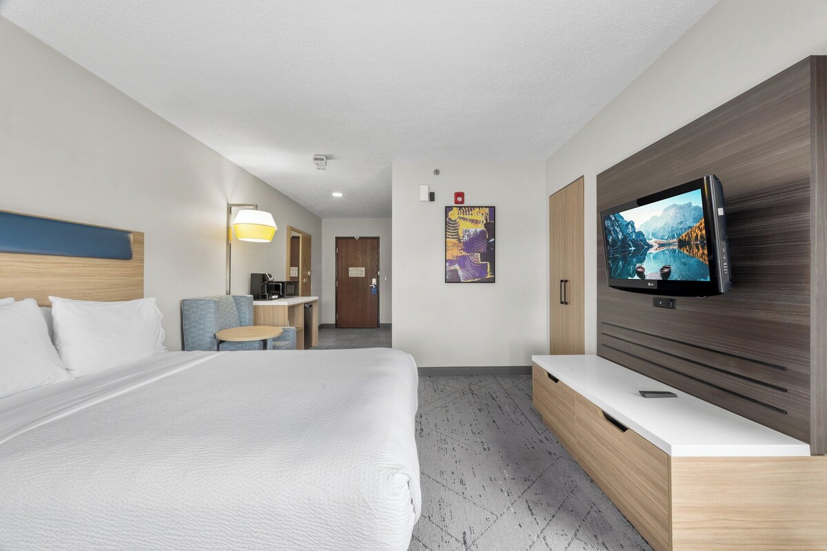 A modern hotel room with a large bed, a desk, a chair, a TV, and a bathroom door.