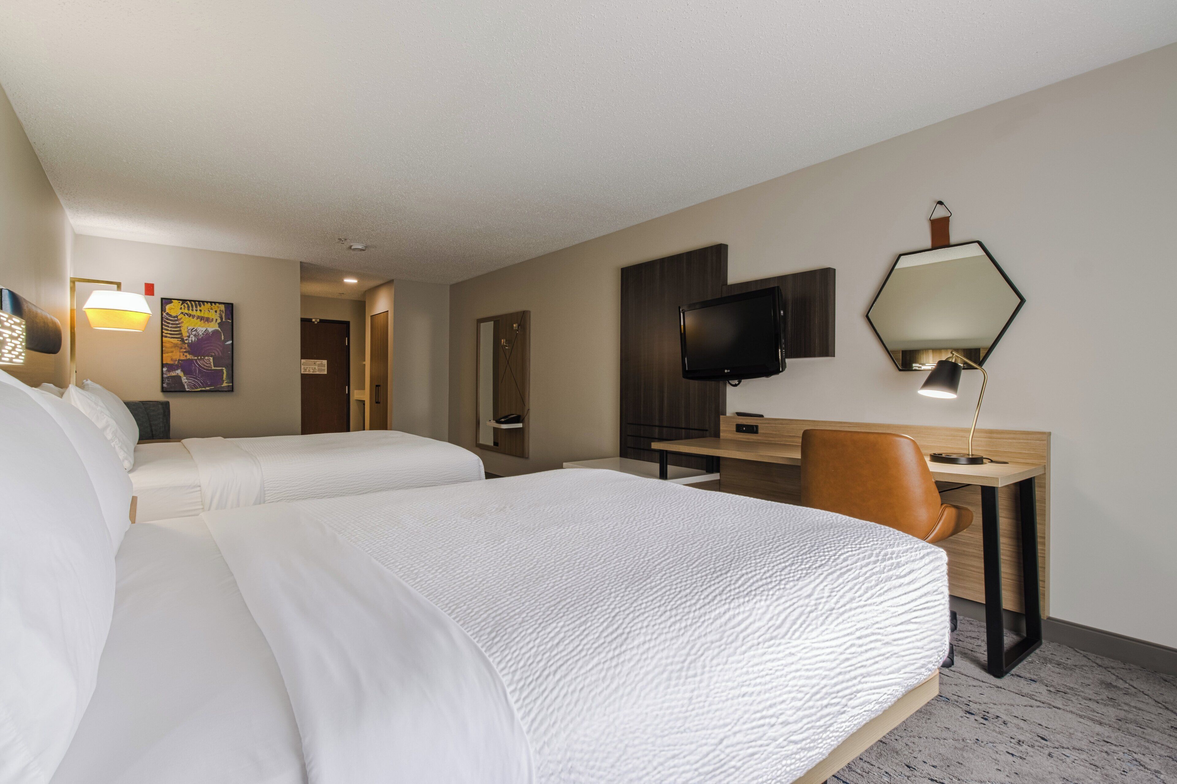 Una habitación de hotel con dos camas, un escritorio con silla, un televisor y una lámpara.