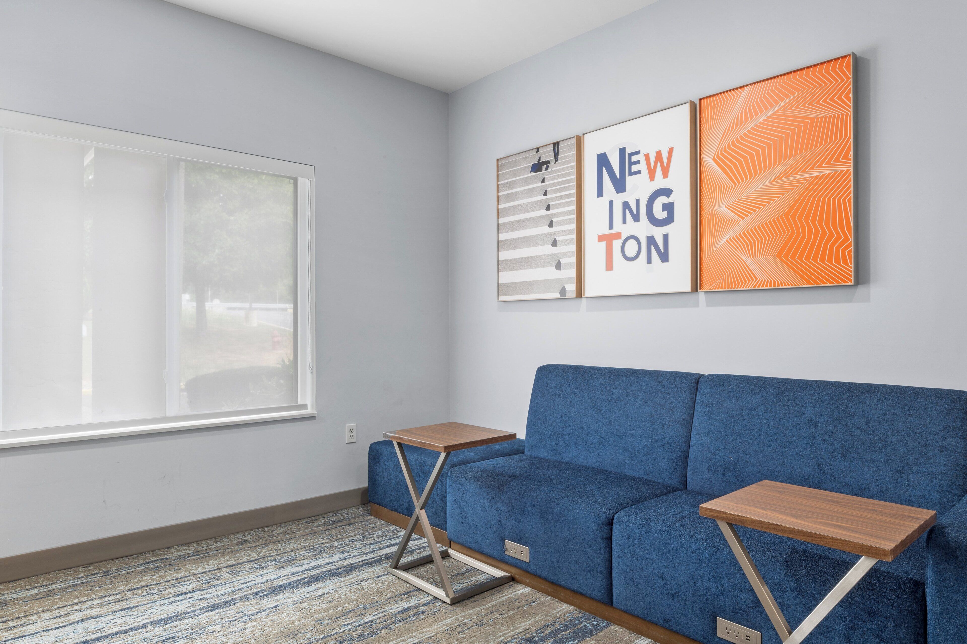 A modern living room with a blue sofa, two wooden side tables, and a large window.