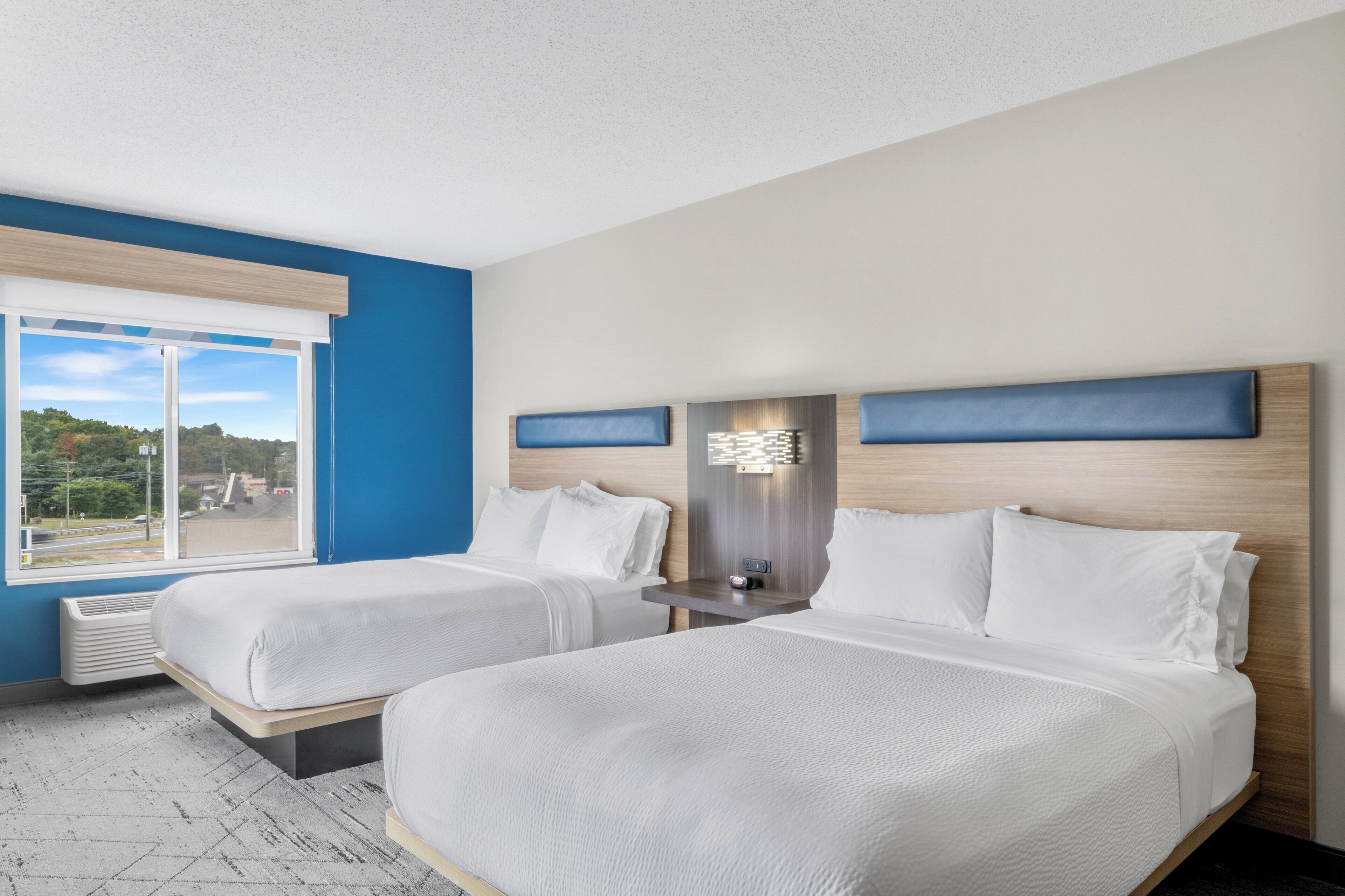 A hotel room with two beds, a large window, and a view of the outdoors.