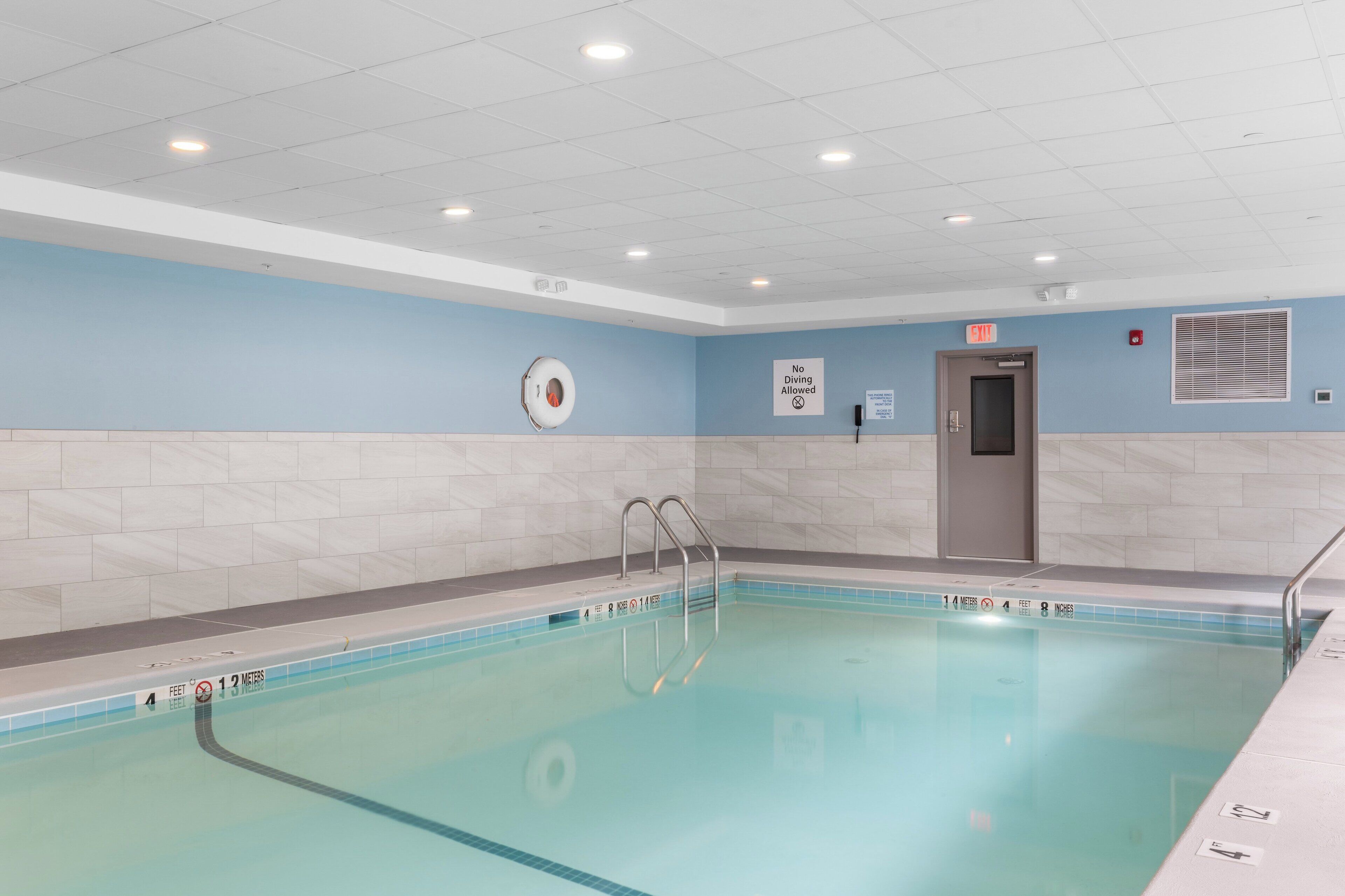 A swimming pool with clear water, a metal ladder, and a sign indicating no diving allowed.