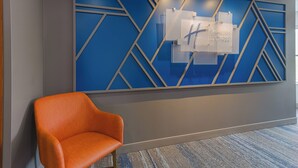 Ein moderner Empfangsbereich mit blauem, geometrischem Wanddesign, einem gut sichtbaren Schild mit der Aufschrift "Holiday Inn Express" und einem einzelnen orangenen Sessel.