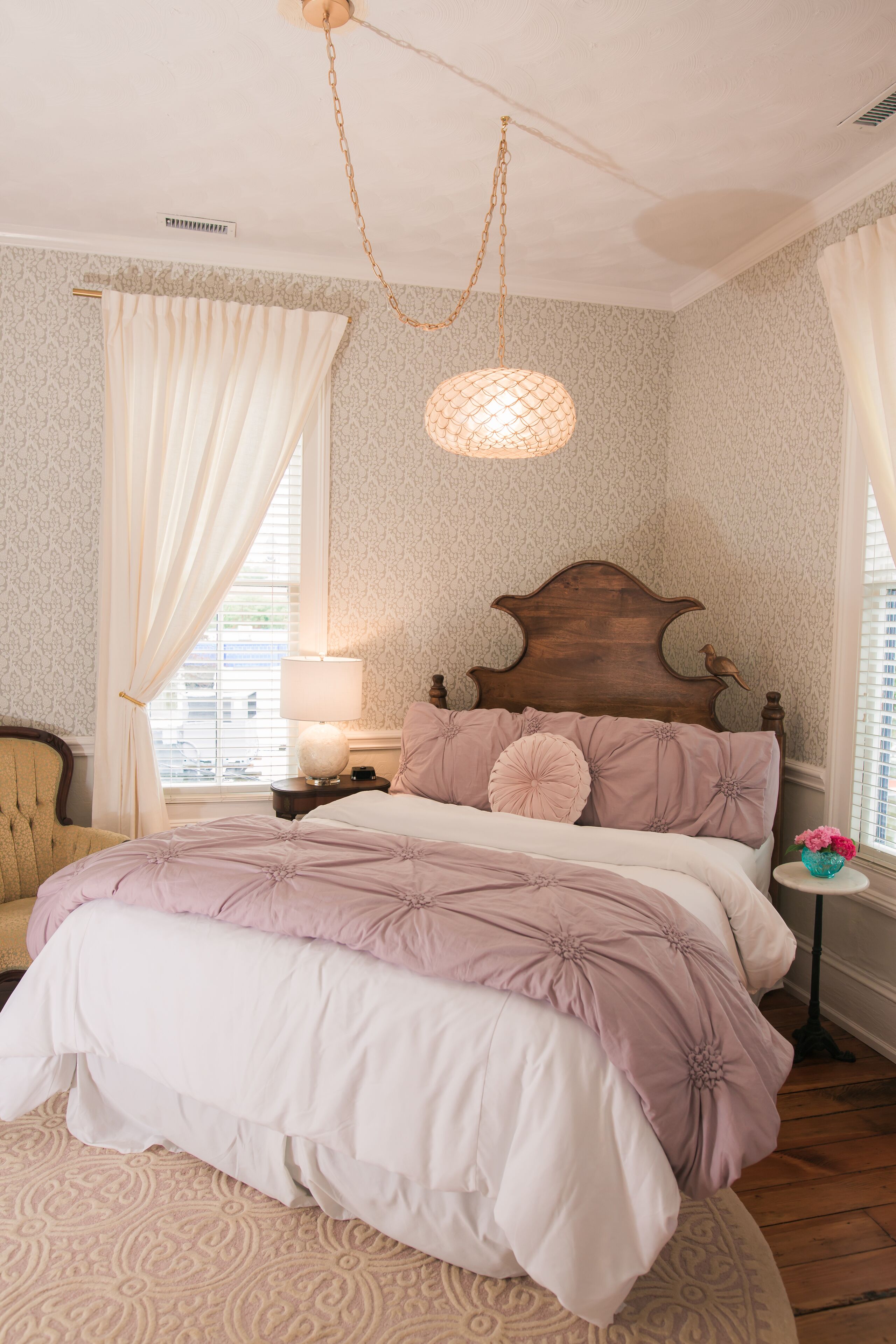 A bedroom with a large bed, a wooden headboard, a nightstand, a lamp, and a window with curtains.