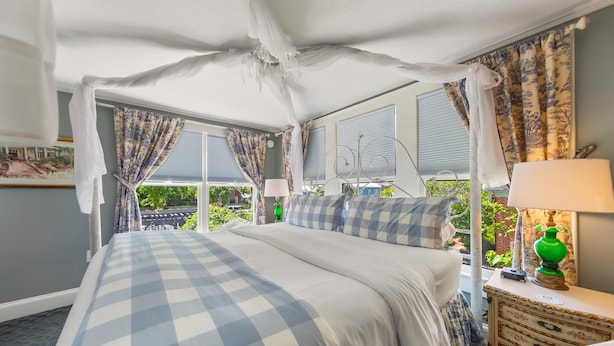 Une chambre à coucher avec un lit à baldaquin, une literie à carreaux, une table de chevet avec une lampe et une vue sur la verdure à l’extérieur.