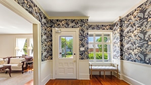 Un couloir avec un plancher en bois, une porte blanche et un papier peint à motifs floraux.