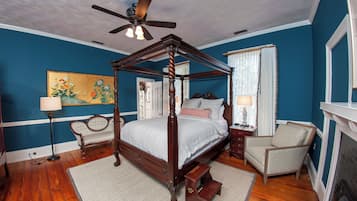 A four-poster bed with a wooden frame, a ceiling fan, and a painting on the wall.