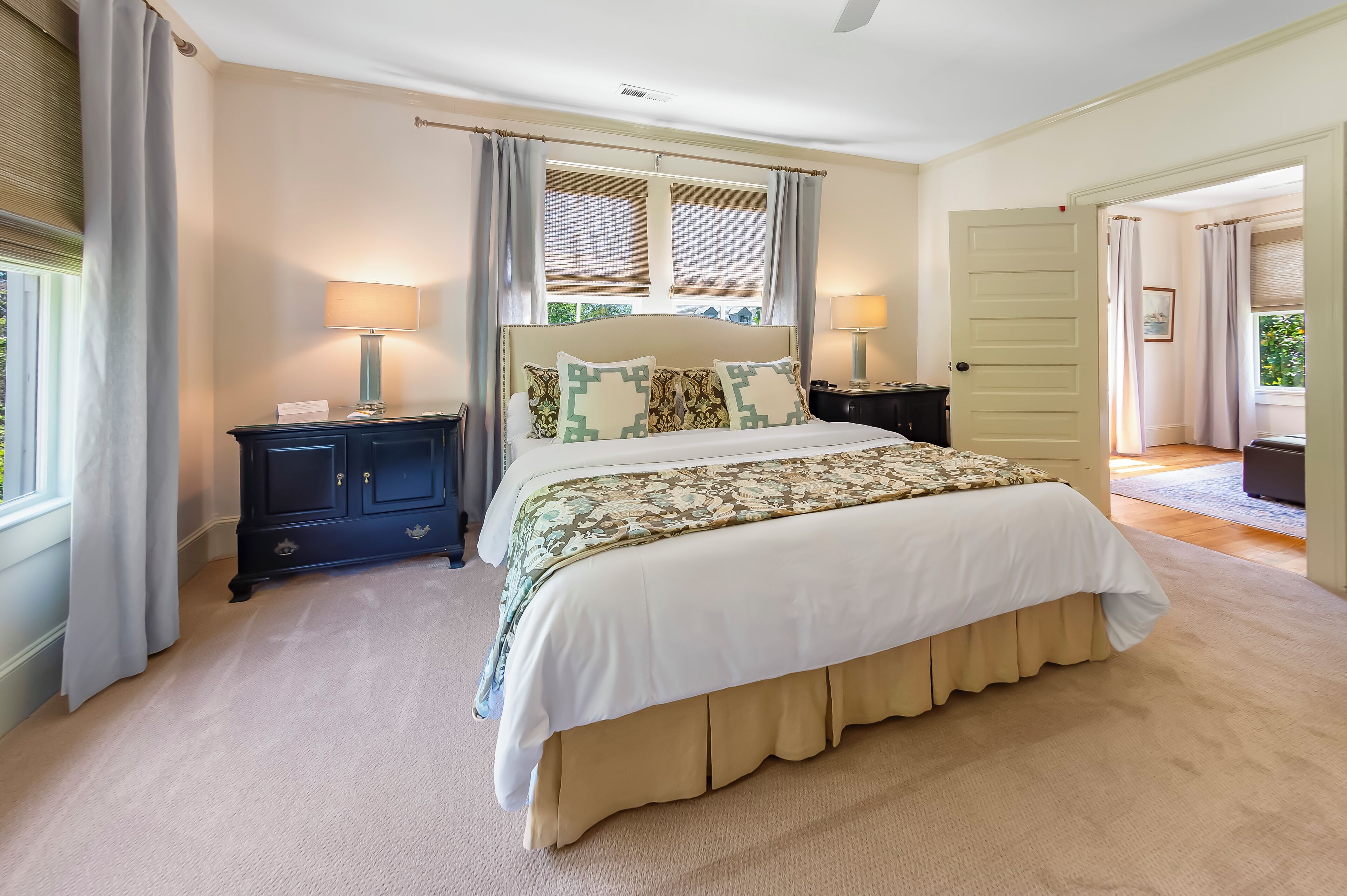 Une chambre à coucher avec un grand lit, deux tables de chevet, une commode et une porte donnant sur une autre pièce.