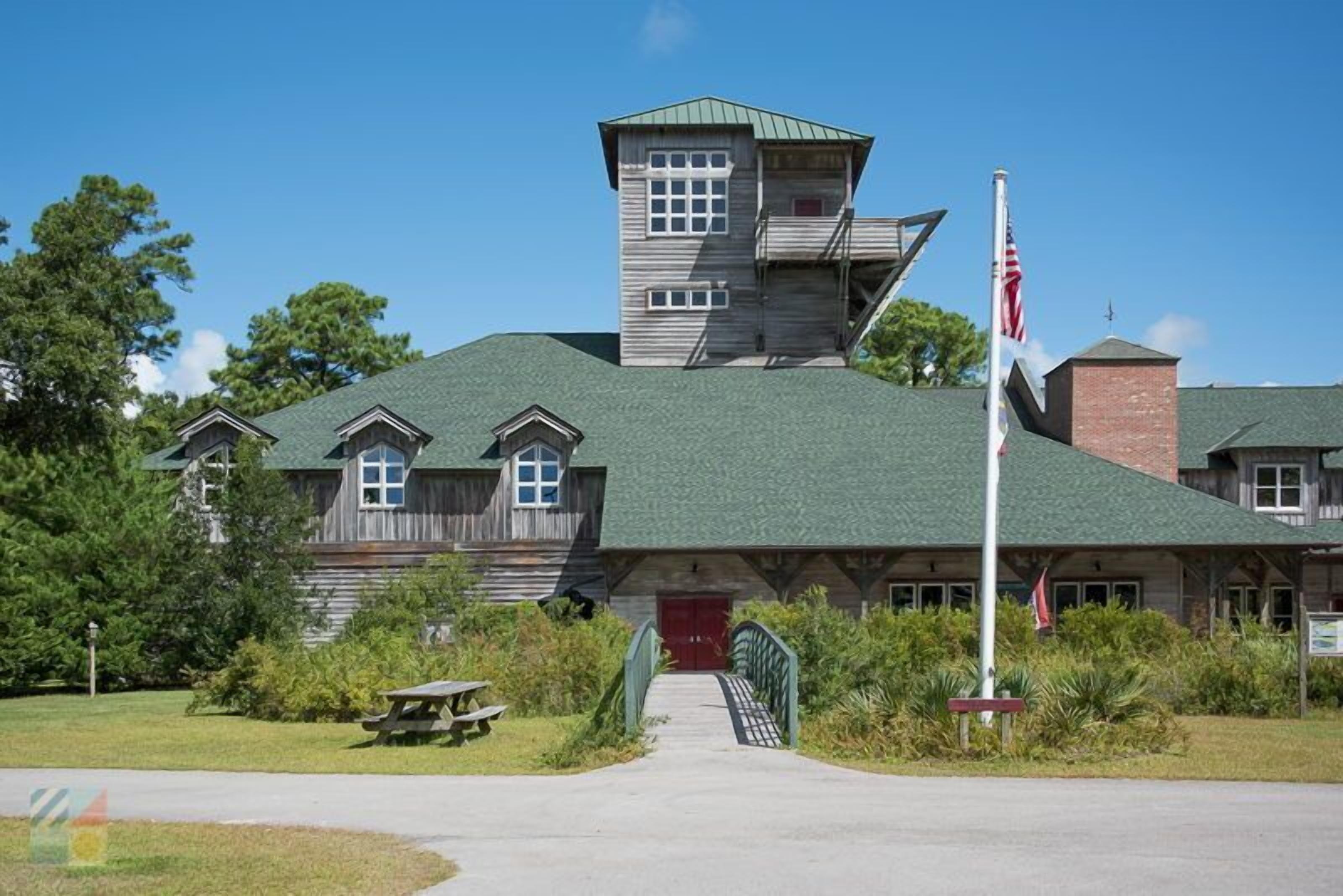 A rustic building with a green roof, a red door, and a flagpole.