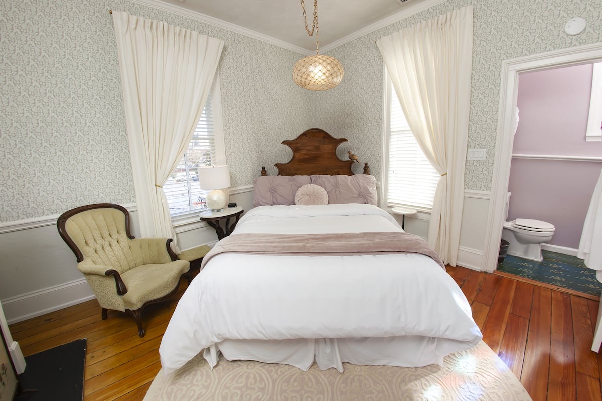 Een slaapkamer met een houten bed, een stoel, een nachtkastje en een hanglamp.