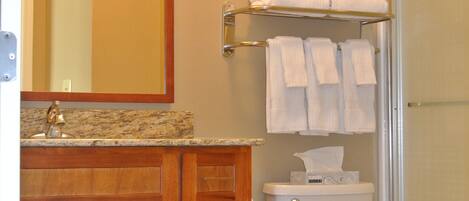 A bathroom with a wooden vanity, a toilet, a glass shower enclosure, and a towel rack.