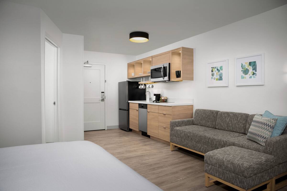 Un espacio habitable compacto con kitchenette, un sofá gris y una cama.