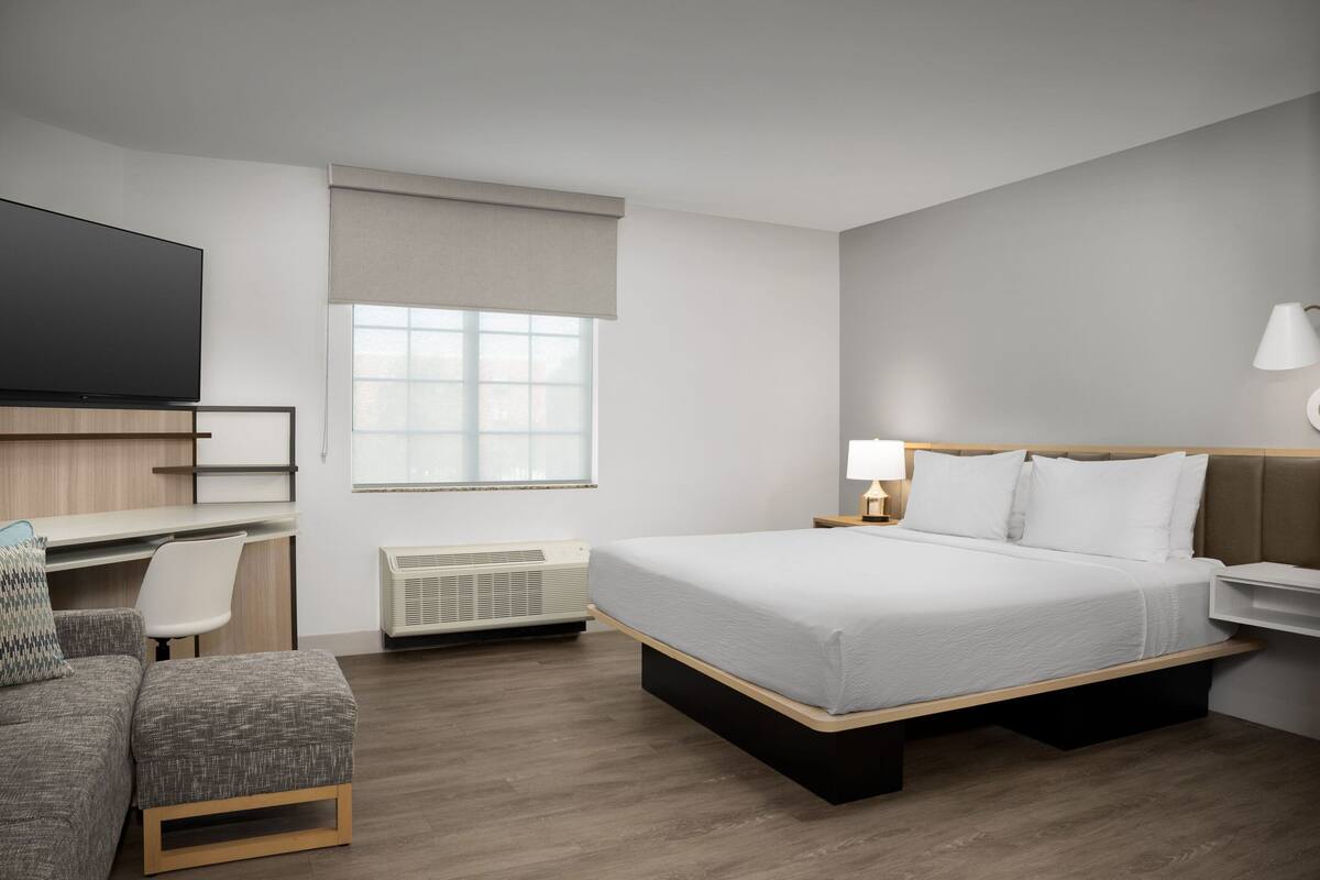 Una habitación de hotel moderna con cama, escritorio, silla, televisor y ventana.