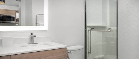 A modern bathroom with a white sink, wooden vanity, toilet, and a glass shower enclosure.