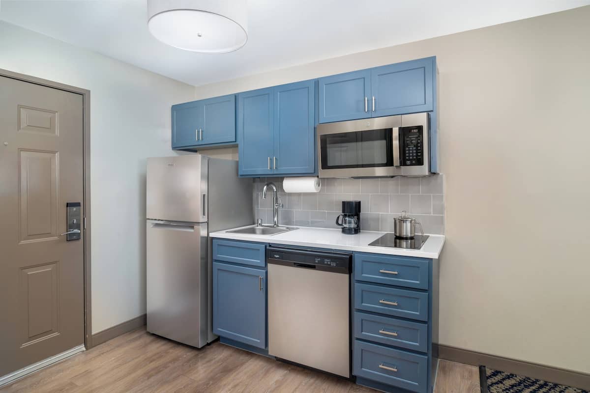 A modern kitchen with blue cabinets, stainless steel appliances, and a white countertop.