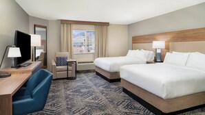 A hotel room with two beds, a desk with a TV, a chair, and a window with a view of buildings.
