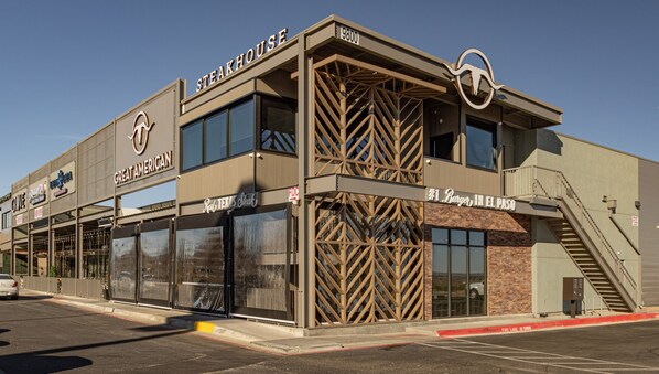 Een steakrestaurant met een modern design, herkenbaar aan een groot logo, meerdere ramen en een vluchttrap.