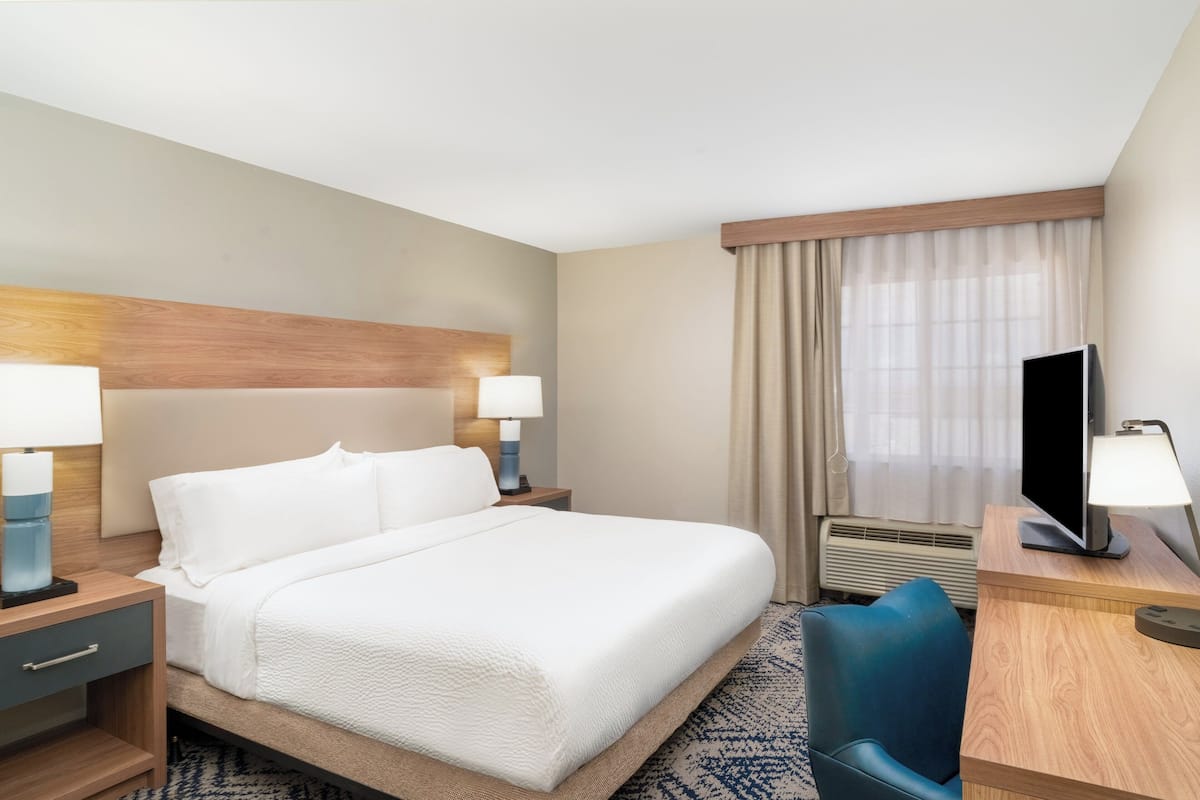 Une chambre d’hôtel avec un grand lit, deux tables de chevet avec des lampes, un bureau avec une télévision et une chaise.