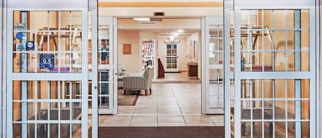 A hotel entrance with automatic sliding doors, a reception area, and a visible staircase.