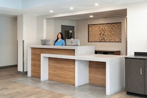 Een receptiebalie met een receptionist, twee laptops en een behang met patroon.